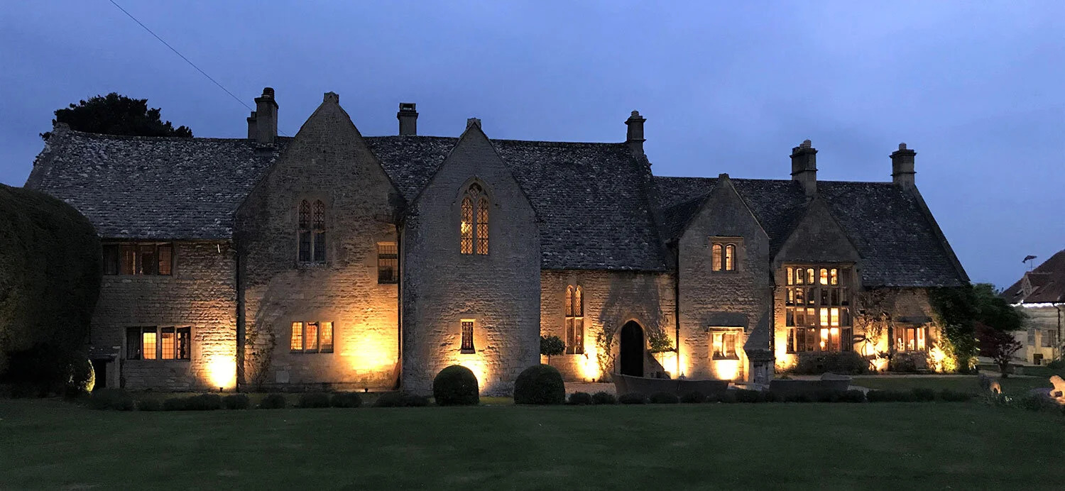 A large stone house illuminated at night, showcasing its architectural details against a dark sky.